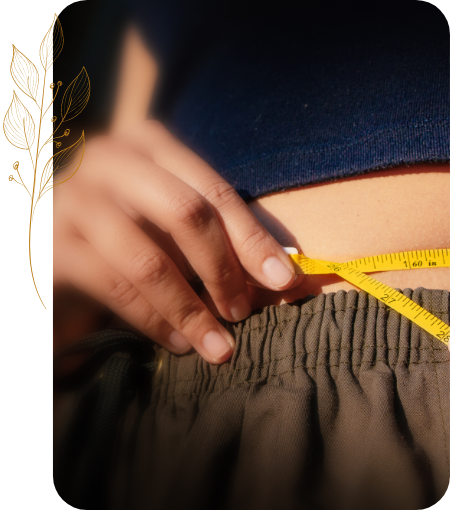 Person holding a tape measure around their waist next to a decorative gold plant