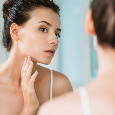 a woman looking at her cheek in the mirror