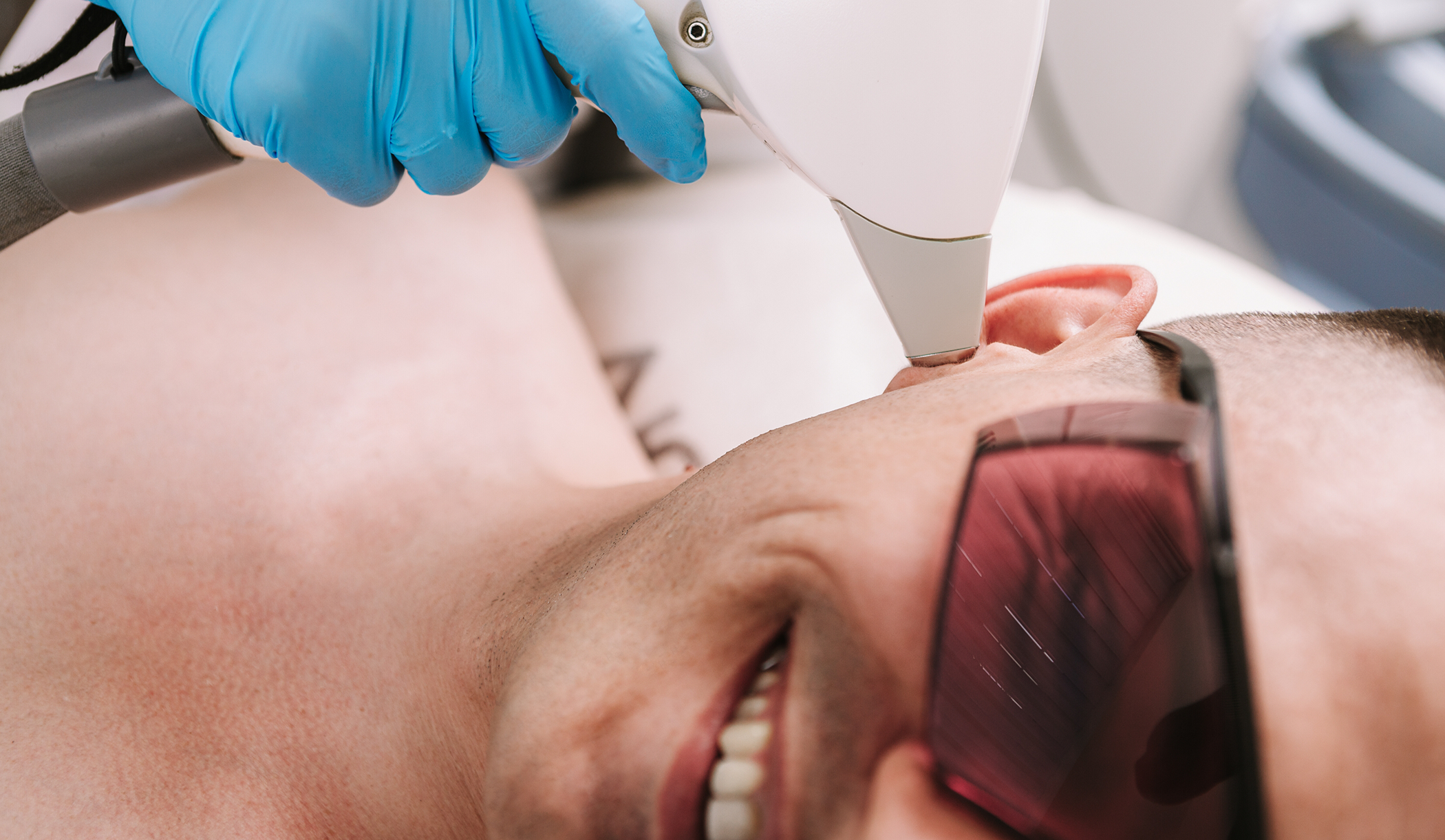Smiling man receiving a laser aesthetic treatment just under his ear